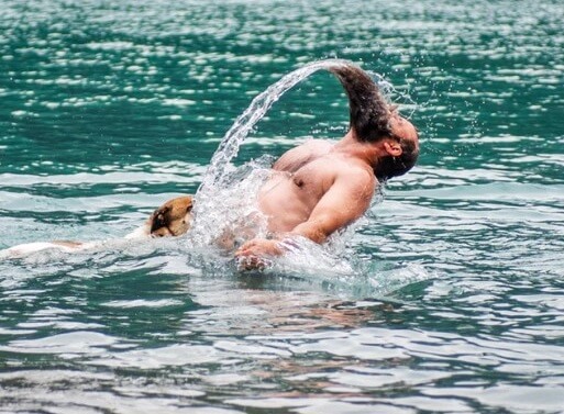גבר משפריץ מים עם הזקן ולידו שוחה כלב